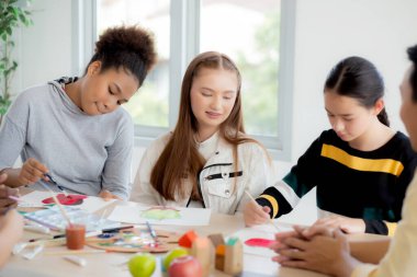 Bir grup öğrenci okulda öğretmenle birlikte oturuyor, çalışıyor ve resim çiziyor, öğrencilerin yaratıcılığı ve gelişimi kursta, okula, eğitim konseptine geri dönüyor..