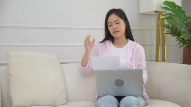 Genç Asyalı kadın, evde, finansal ve fatura mektubunda, iş konseptinde endişeli, mutsuz ve şokta iken, kredi ve gider finansmanı ile ilgili bilgilendirme belgesini okuyarak stresli bir şekilde oturuyor..