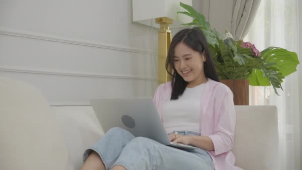 年轻的亚洲女商人从家里的笔记本电脑上网工作到客厅的沙发上工作 自由职业姑娘坐在沙发上舒舒服服 生活方式的概念 — 图库视频影像