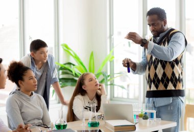 Genç öğretmen grup öğrencilerine okulda sıvı için bilim ve test kimyasalları öğretiyor, çocuklar laboratuarda deney bilimi okuyor ve öğreniyor, eğitim konsepti.