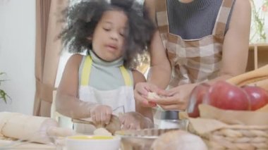 Annesi önlüklü Afrikalı bir aile kızıyla mutfakta yemek pişirmek için taze un sürüyor, ebeveyn ve küçük çocuk yemeklerini eğlenceli ve eğlenceli bir şekilde hazırlıyorlar..