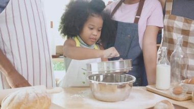 African America family wearing apron for cooking bakery or bread with flour together in the kitchen at home, parent and little child preparing food with fun and playful, relationship and hobby.