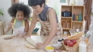 Annesi önlüklü Afrikalı bir aile kızıyla mutfakta yemek pişirmek için taze un sürüyor, ebeveyn ve küçük çocuk yemeklerini eğlenceli ve eğlenceli bir şekilde hazırlıyorlar..