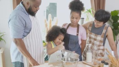 African America family wearing apron for cooking bakery or bread with flour together in the kitchen at home, parent and little child preparing food with fun and playful, relationship and hobby.