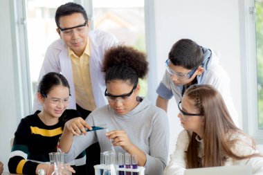 Genç öğretmen grup öğrencilerine okulda sıvı için bilim ve test kimyasalları öğretiyor, çocuklar laboratuarda deney bilimi okuyor ve öğreniyor, eğitim konsepti.