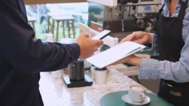 Müşterinin elleri, akıllı telefon taraması QR kodunu kafe kasiyerine ödeme yapmak için kullanırken, personel tablet kullanırken internet bankacılığı, iş ve teknoloji ile işlem kavramı hakkında müşteri ödemesi yapıyor..