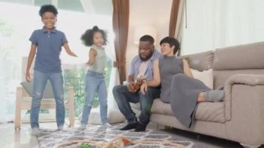 Mutlu aile babası ukulele ya da gitar çalıyor ve anne ve çocuklar birlikte şarkı söylüyor ve eğlenerek dans ediyorlar ve evde oturma odasında eğleniyorlar, ebeveyn ve çocuğun hobisi dinlenmek için..