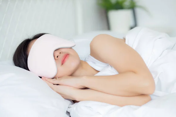 Beautiful young asian woman wearing cover eye and sleeping on bed with head on pillow comfort and happiness in the bedroom at home, girl with relax and leisure for wellness, lifestyles concept.