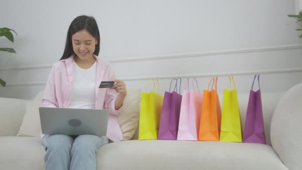 年轻的亚洲女人坐在沙发上 用笔记本电脑上网购物 用信用卡上网购物 快乐的女孩子用金融 购物和付款 商业概念来支付 — 图库视频影像