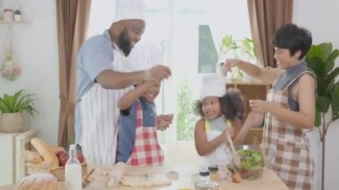 Afro-Amerikan ailesi yemek pişirmek ve dans etmek için önlük takıyor. Mutfakta birlikte eğleniyorlar. Ebeveynler ve küçük çocuklar yemeklerini eğlenceli ve eğlenceli bir şekilde hazırlıyorlar..
