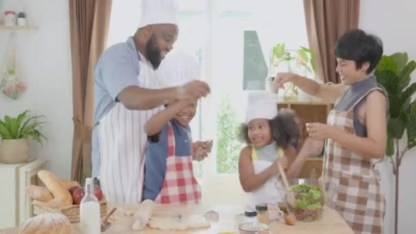 アフリカ系アメリカ人の家族は 家庭で一緒に台所で一緒に料理や踊りのためにエプロンを身に着けています 楽しさと遊び心のある料理を準備親と小さな子供 国内生活 — ストック動画