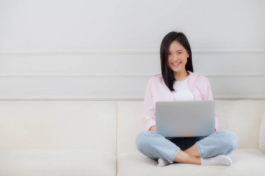 Genç Asyalı iş kadını evde dizüstü bilgisayarla çalışıyor oturma odasındaki kanepede internete bağlanıyor, defter kullanan serbest bir kız rahat ve rahat bir şekilde kanepede oturuyor, yaşam tarzı kavramı..