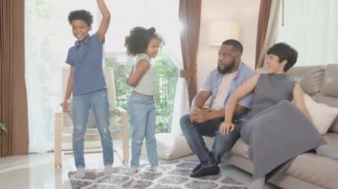 Mutlu aile babası ukulele ya da gitar çalıyor ve anne ve çocuklar birlikte şarkı söylüyor ve eğlenerek dans ediyorlar ve evde oturma odasında eğleniyorlar, ebeveyn ve çocuğun hobisi dinlenmek için..