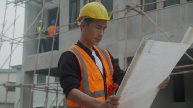 İnşaat şantiyesinde, inşaatta, müteahhitte veya inşaatçıda başarılı olmak için projeyi denetlemek ve planlamak için sağlam görünümlü planlar giyen mimar veya mühendis..