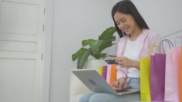 年轻的亚洲女人坐在沙发上 用笔记本电脑上网购物 用信用卡上网购物 快乐的女孩子用金融 购物和付款 商业概念来支付 — 图库视频影像