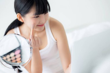 Laptop bilgisayarında yanağına fırça sürerek makyaj yapmayı öğrenen genç Asyalı bir kadın. Yatakta özel ders veren, öğretmenlik yapan ve sosyal medyada makyaj yapan bir kadın..