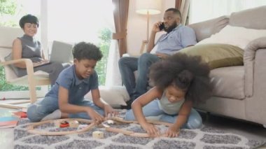 Mutlu Afrikalı aile babası ve anne çalışıyor ve çocuklar oturma odasında eğlence ile oyuncak demiryolu oynuyorlar, çocuk rahatlıyor ve eğitimle gelişiyor, etnik çeşitlilikle.
