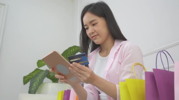 年轻的亚洲女人坐在沙发上 用数码平板电脑在线购物 用信用卡上网购物 快乐女孩用金融交易 购物和付款 商业概念来支付 — 图库视频影像