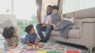 Mutlu Afrikalı aile babası ve anne çalışıyor ve çocuklar oturma odasında eğlence ile oyuncak demiryolu oynuyorlar, çocuk rahatlıyor ve eğitimle gelişiyor, etnik çeşitlilikle.