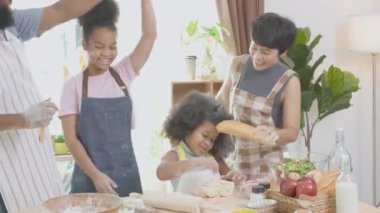 Afro-Amerikan ailesi yemek pişirmek, dans etmek ve şarkı söylemek için önlük takıyor. Anne ve baba ve küçük çocuk, eğlenceli ve neşeli bir şekilde yemek ve şarkı hazırlıyorlar..