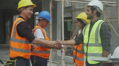 Asyalı genç ustabaşı ve işçilerden oluşan bir ekip el sıkışarak başarı, mühendis ve inşaat sahası için takım çalışması yapıyor. Mimarlar anlaşma ve anlaşma için el sıkışıyor..