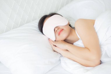 Güzel Asyalı genç bir kadın örtülü göz takıyor ve yatak odasında başı yastıkta uyuyor rahatlık ve mutlulukla, rahatlık ve rahatlık için boş vakti olan bir kız, yaşam tarzı konsepti..