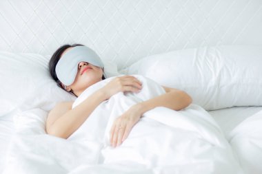 Güzel Asyalı genç bir kadın örtülü göz takıyor ve yatak odasında başı yastıkta uyuyor rahatlık ve mutlulukla, rahatlık ve rahatlık için boş vakti olan bir kız, yaşam tarzı konsepti..