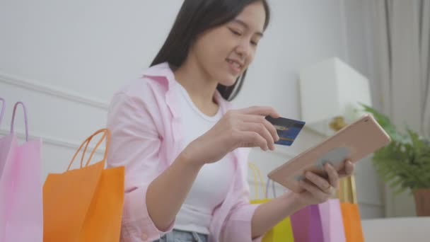年轻的亚洲女人坐在沙发上 用数码平板电脑在线购物 用信用卡上网购物 快乐女孩用金融交易 购物和付款 商业概念来支付 — 图库视频影像