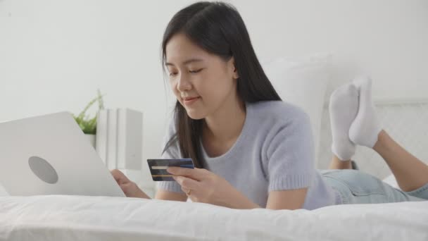 年轻的亚洲女人躺在床上 用笔记本电脑在网上购物 用信用卡上网 快乐女孩在卧室用电子商务支付 支付和交易金融 商业概念 — 图库视频影像