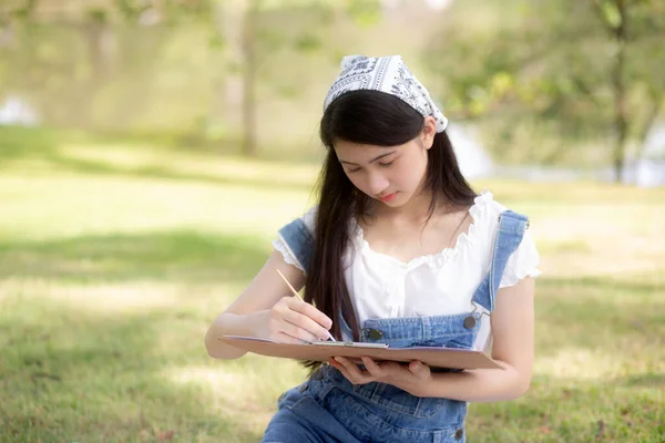 Young asian woman sitting drawing picture with colorful paint brush while leisure in the park on summer, artist and skill with expertise, girl drawing with talent is hobby, lifestyles concept.