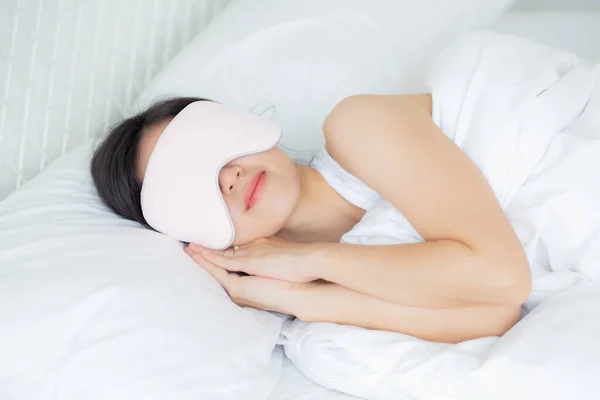 Beautiful young asian woman wearing cover eye and sleeping on bed with head on pillow comfort and happiness in the bedroom at home, girl with relax and leisure for wellness, lifestyles concept.