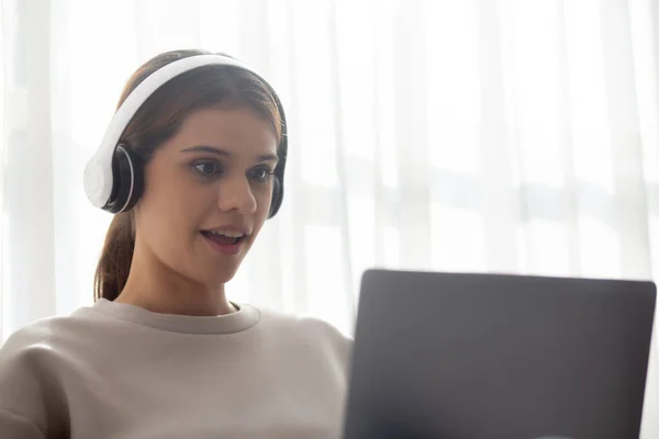 Happy young woman wearing headphones listening music while using laptop computer and singing with fun and enjoy in the living room, happiness female with entertainment, lifestyles concept.