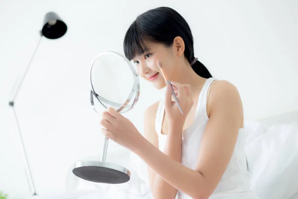 美しい若いアジアの女性は ベッドの上の化粧鏡の頬のメイクにブラシを適用します ベッドルームで肌の顔やしわを持つ少女の美しさ 女性のための化粧品 スキンケアコンセプト — ストック写真