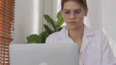 Young woman doctor working while looking document on clipboard and using laptop computer at clinic, female signing on paperwork and using notebook at hospital, one person, medical concept.