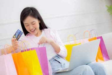 Mutluluk genç Asyalı kadın kanepeye oturmuş evde kredi kartıyla online alışveriş yaparken, heyecanlı, alışveriş düşkünü ve yaşam tarzı konsepti olan tüketici indirimi ve alışverişi yaparken..