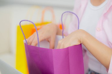 Closeup hands of woman sitting on sofa open paper bag while online shopping with credit card at home, girl purchase and discount of consumer with excited, shopaholic and lifestyles concept.