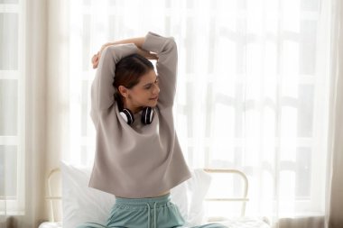 Beautiful young woman waking up in the morning and stretching sitting on bed in the bedroom at home, girl is a cozy with fresh happiness and smile, wellbeing and health concept.