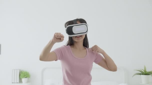年轻的亚洲女人戴着Vr耳机玩游戏 在卧室里兴奋地躺在床上 女人用虚拟现实或多样化创新来模拟3D 生活方式和技术概念 — 图库视频影像
