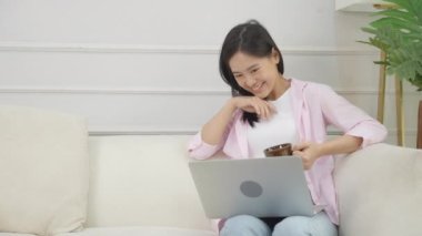 Young asian business woman work from home with laptop computer and drinking coffee on sofa in living room, freelance girl using notebook sitting on couch with comfort and relax, lifestyles concept.