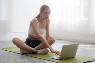 Evde dizüstü bilgisayar dersi izlerken, spor yaparken egzersiz ya da yoga yapan genç bir kadın, antrenman için motivasyon defteri arayan bir kadın, bir kişi, yaşam tarzı ve spor konsepti..