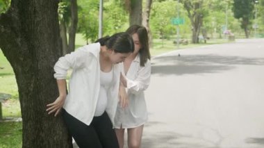 Genç Asyalı hamile kadın karın ağrısı çekerken, insanlar parkta, annelikte ve yardımda, hamilelikte ve sağlıkta, sağlık hizmetlerinde ve hastalıkta, yaşam tarzlarında,.