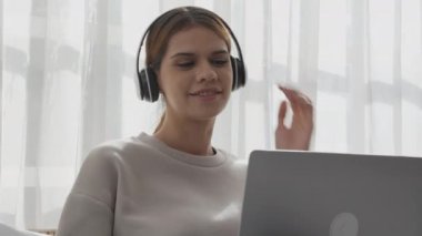 Happy young woman wearing headphones listening music while using laptop computer and singing with fun and enjoy in the living room, happiness female with entertainment, lifestyles concept.