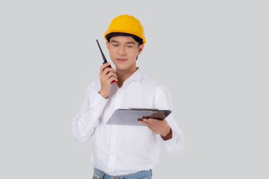 Portrait young asian man is engineer wearing helmet standing and using radio for speak with confident while holding report document isolated on white background, male is architect or contractor.