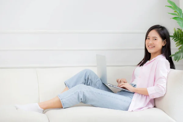 Young asian business woman work from home with laptop computer online to internet on sofa in living room, freelance girl using notebook sitting on couch with comfort and relax, lifestyles concept.