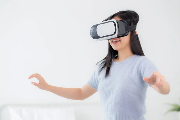 Young asian woman wearing vr headset playing game with excited in the bedroom at home, female using virtual reality or metaverse innovation for simulation 3D, lifestyles and technology concept.