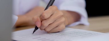 Closeup hands of doctor woman signing on document paper at clinic, close-up hands of physician female writing about contract or result of diagnostic for recording, medical and life insurance concept.