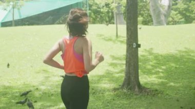 Genç Asyalı güzel bir kadın yazın parkta koşuyor ya da koşuyor. Bahçede tropik sporla rahatlamak için kız egzersizi yapıyor. Bir kişi, sağlık ve spor kavramı..