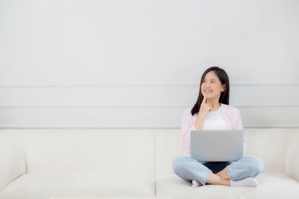自宅のリビングルームでソファに座っているラップトップコンピュータ上で働く若いアジアの女性 女性はノートブックを使用してソファに座ってフリーランスであり 決定についての疑い ライフスタイルの概念 — ストック写真