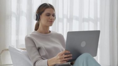 Kulaklık takan, müzik dinleyen, dizüstü bilgisayarla şarkı söyleyen ve oturma odasında eğlenen, eğlence ve yaşam tarzı olan mutlu bir kadın..