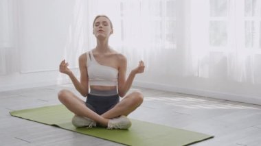 Yoga yapan ve rahatlamak için meditasyon yapan genç bir kadın. Evde paspas üzerinde hayatı dengeleyen bir kadın. Rahatlama, sağlık ve spor konsepti için kadın oturma ve egzersiz yogası..